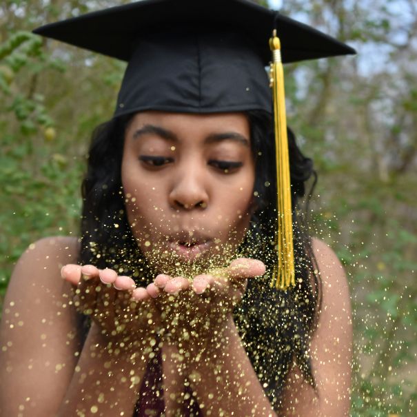 New graduate blowing gold glitter while wearing graduation cap